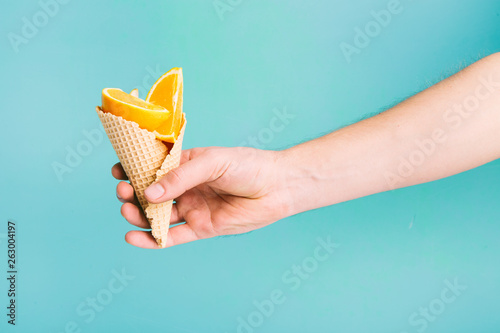 Fresh Orange cut in ice cream cone on blue pastel background. Hand holding fruits. 