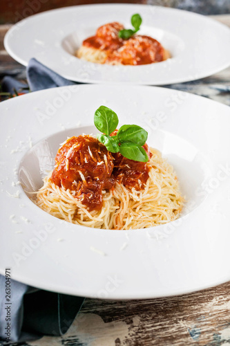 Close-Up meatballs in tomato sauce with spaghetti on white plates, cherry tomatoes on a wooden table.