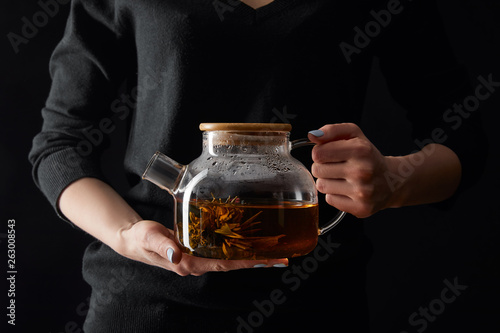 cropped view of young woman holding transparent teapot with chinese blooming tea isolated on black