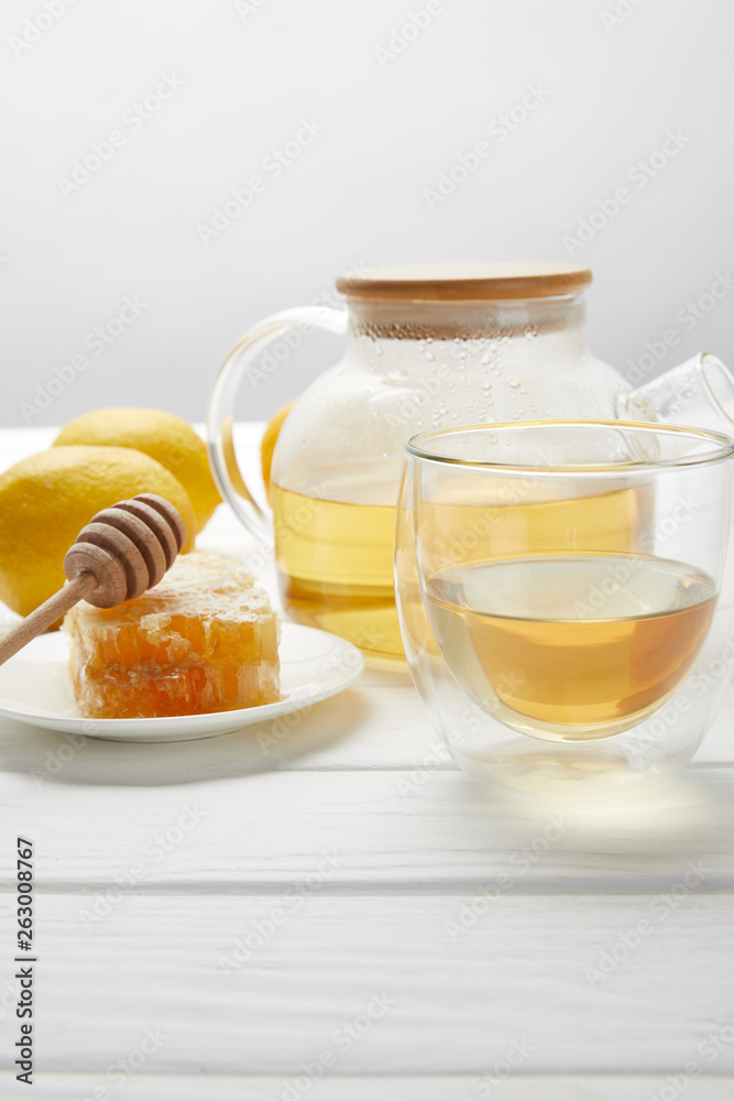 teapot with organic herbal tea, glass, lemons and honeycomb on white wooden table
