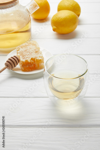 transparent glass and teapot with green tea, lemons and honeycomb on white wooden table