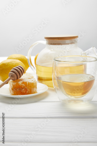 teapot with organic herbal tea, glass, lemons and honeycomb on white wooden table