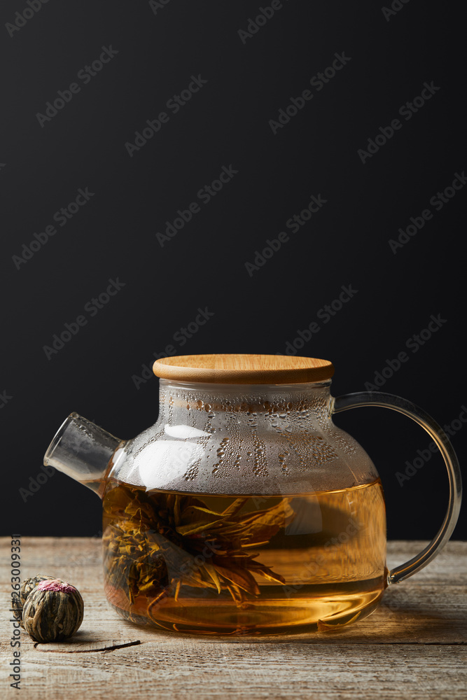 transparent teapot with blooming tea and tea balls on wooden table isolated on black with copy space transparent teapot with blooming tea and tea balls on wooden table isolated on black with copy space