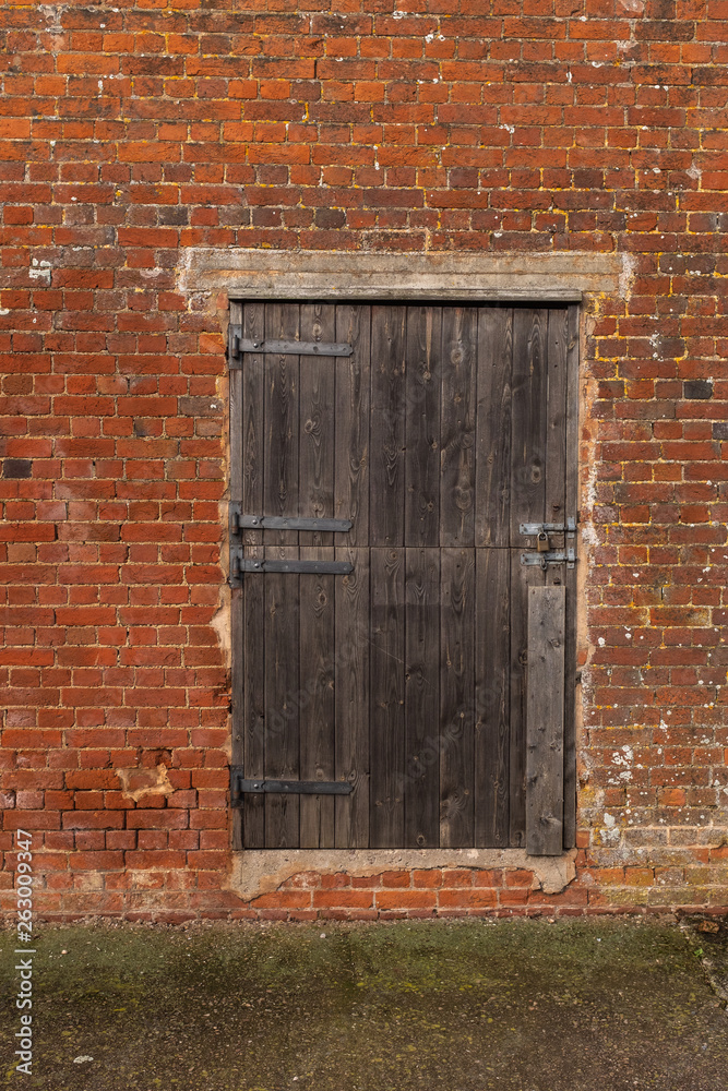 A close up of a wooden seasoned barn door in a brick wall of a out building on a farm