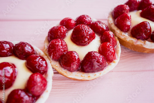 three fresh bright and beautiful cakes panna cotta with butter cream and raspberries close-up diagonally on a delicate pink wooden background