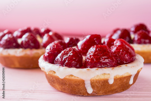 several panna cotta cakes with cream and raspberries close up on a gentle pink wooden background