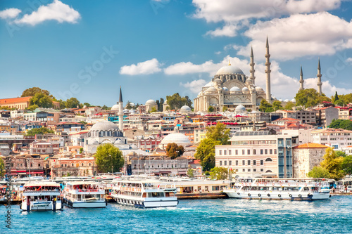 Touristic sightseeing ships in Golden Horn bay of Istanbul and view on Suleymaniye mosque with Sultanahmet district against blue sky and clouds. Istanbul, Turkey during sunny summer day.