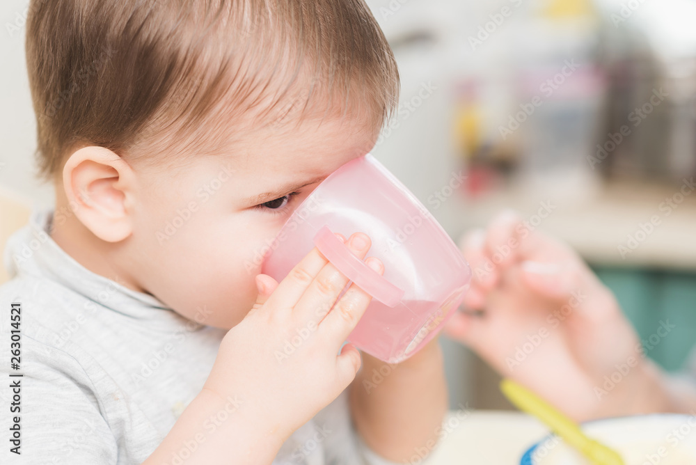 child in the kitchen drinking from a cup of water child in the kitchen drinking from a cup of water