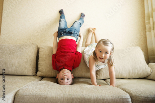 Brother and sister playing on the couch: the boy stands upside down photo