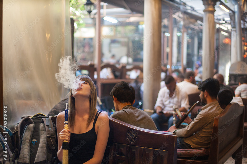 woman smoking shisha at turkey restaurant. young girl exhaling smoke with closed eyes. Closeup photo of girl smoking traditional hookah pipe. Woman exhaling smoke in old hookah cafe.