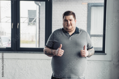 overweight tattooed man in grey t-shirt Looking At Camera and showing thumbs up photo