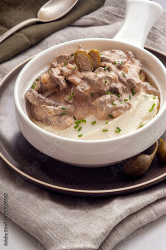 Beef stroganoff with mashed potatoes. The traditional dish of Russian cuisine. Beef meat in a thick sauce on sour cream. Serve on a deep white plate. Close up and vertical view.