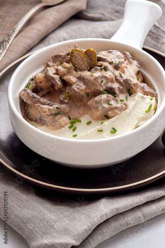 Beef stroganoff with mashed potatoes. The traditional dish of Russian cuisine. Beef meat in a thick sauce on sour cream. Serve on a deep white plate. Close up and vertical view.