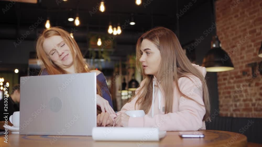 Two beautiful young business women sitting at table in cafe and discussing presentation on laptop computer over coffee Two beautiful young business women sitting at table in cafe and discussing presentation on laptop computer over coffee