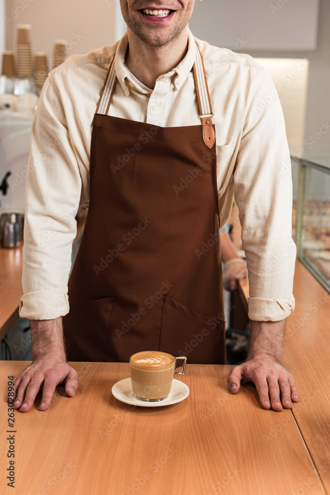 Φωτογραφία Cropped view of laughing barista in brown apron with cup of coffee
