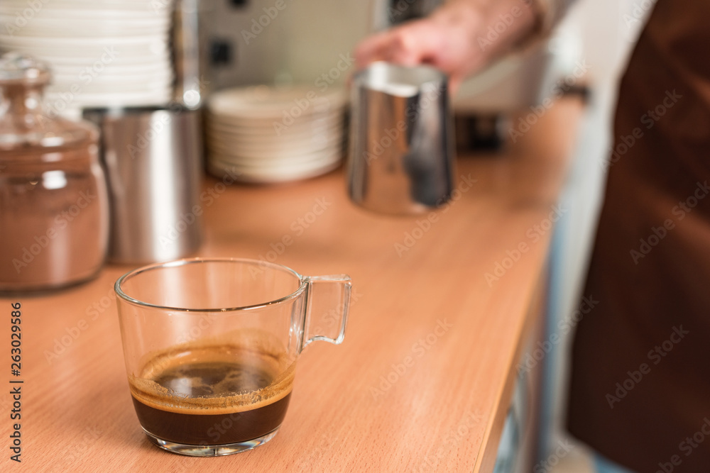 Φωτογραφία Cropped view of barista with milk jug and cup of coffee on wooden table