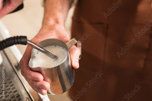 Cropped view of barista filling up steel milk jug