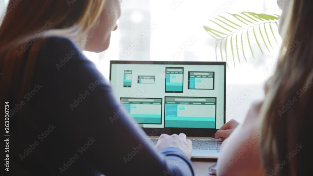 Rear view of two unrecognizable female professionals discussing website design for different devices presented on laptop screen sitting at desk (ATTN templates designed by ME)