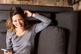 Beautiful and happy young woman with smartphone smiling on sofa