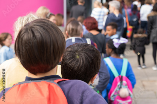 Big queue of parents and children near to school entrance. It`s an Open Doors Day in a School. Focus is on the one boy's head back in the queue. Welcome to school!