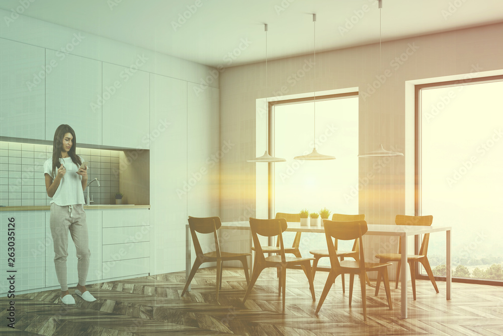 Fototapeta premium Woman with phone in white kitchen with table
