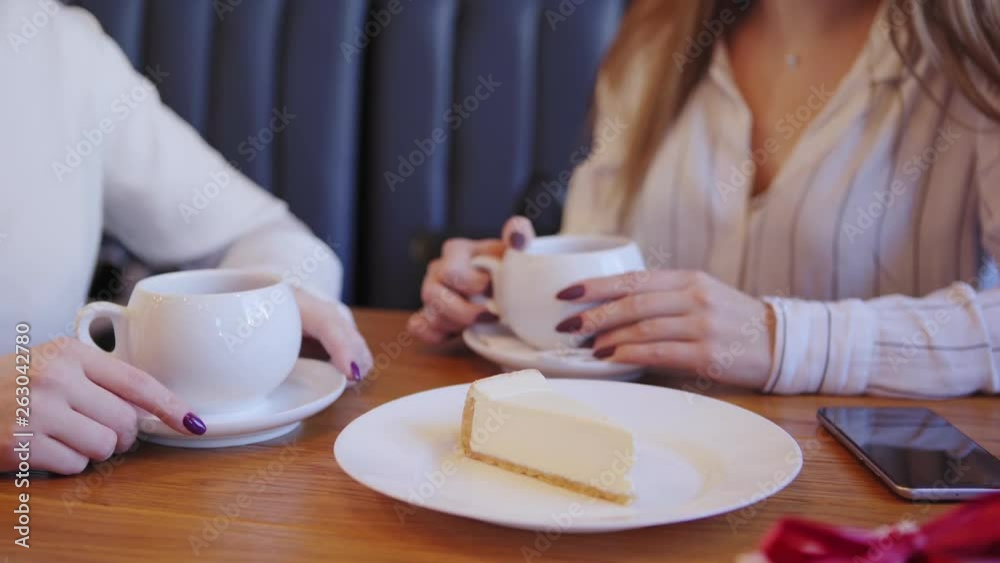 Hands of waitress bringing cheesecake for woman having coffee with friend as cafe birthday compliment. Gift boх and smartphone on table Hands of waitress bringing cheesecake for woman having coffee with friend as cafe birthday compliment. Gift boх and smartphone on table