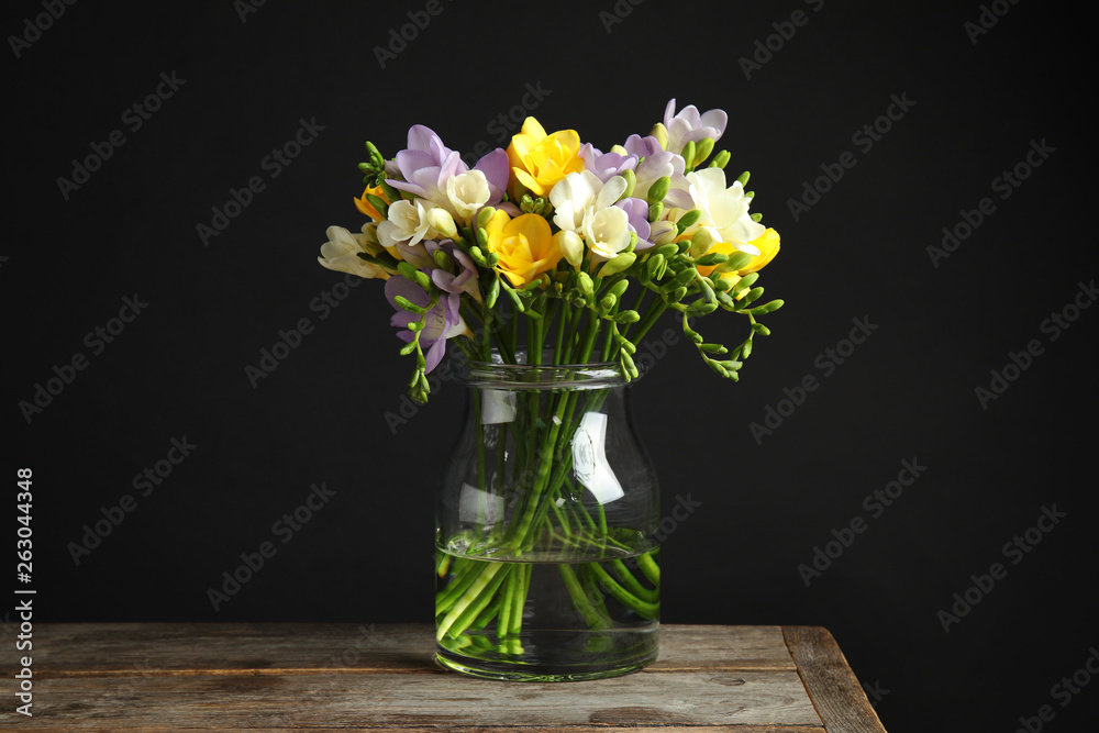 Bouquet of fresh freesia flowers in glass vase on table against black background