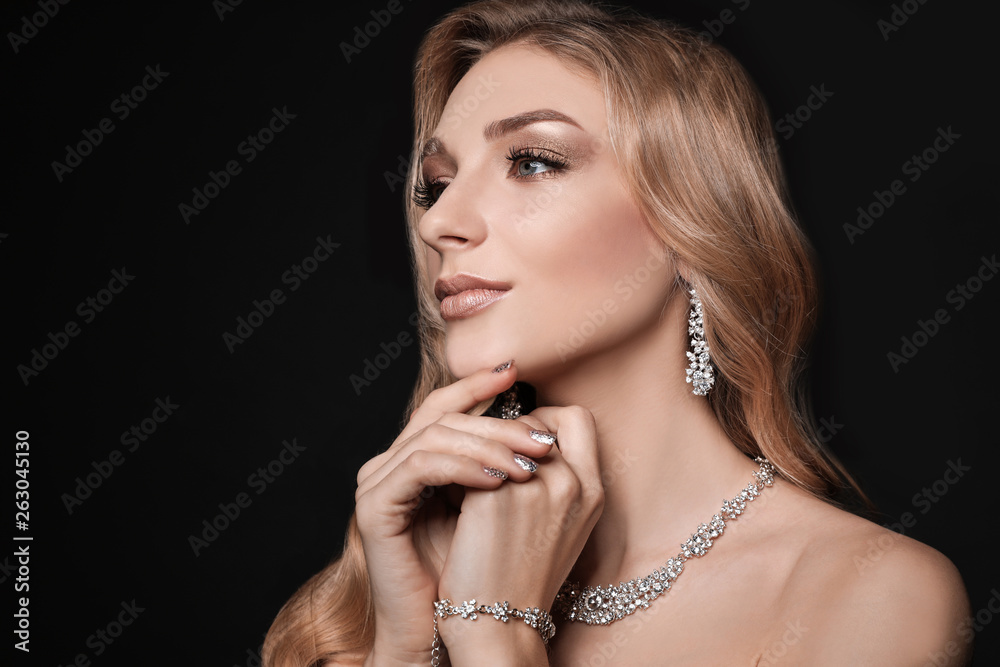 Beautiful young woman with elegant jewelry on dark background. Space for text