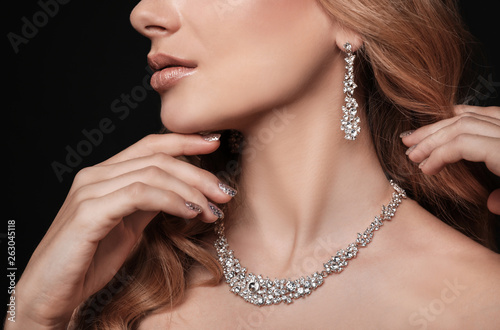 Beautiful young woman with elegant jewelry on dark background, closeup