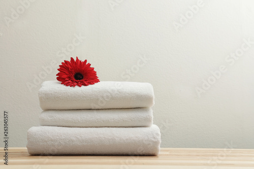 Stack of fresh towels with flower on table. Space for text