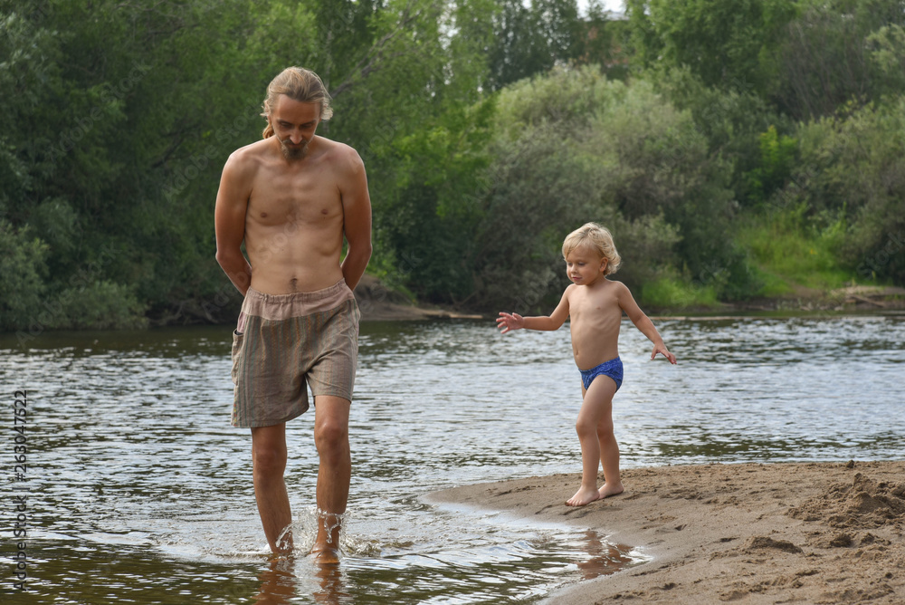 Fototapeta premium Father and son on the beach. Happy family. river. happy family on the beach. swimming. hot summer day. vacation. coach. father's day. blond boy.