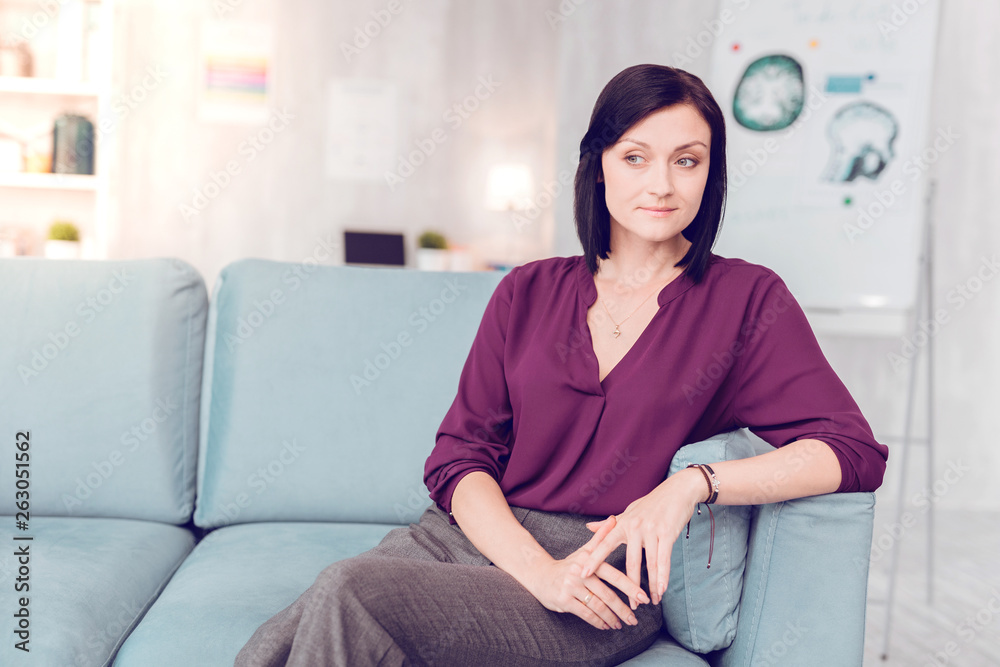 Beautiful dark-haired elegant woman sitting on a living room couch. Beautiful dark-haired elegant woman sitting on a living room couch.
