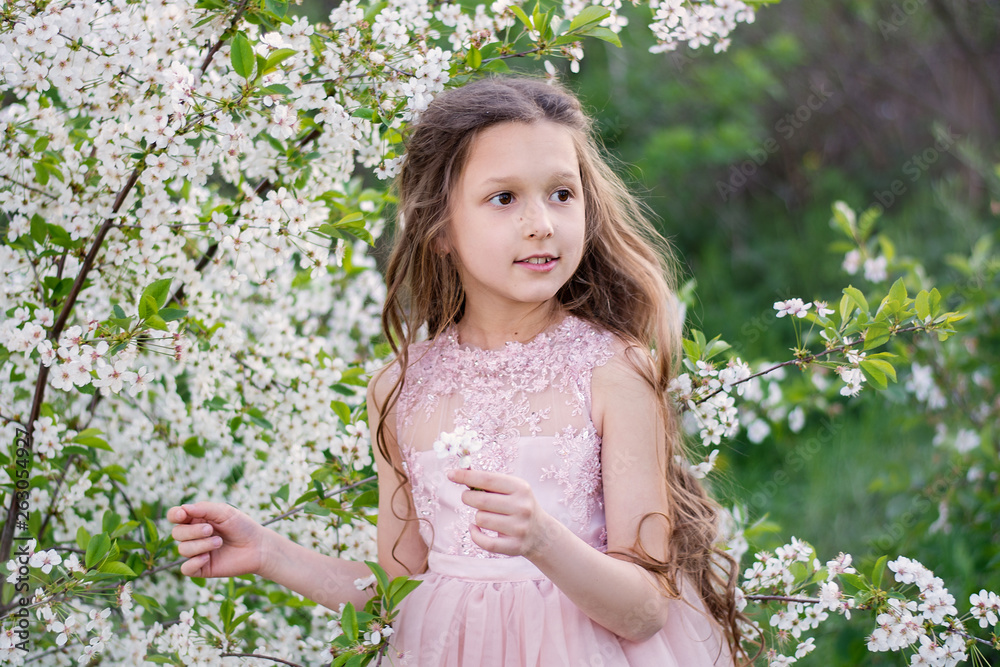 A beautiful baby is smiling. Girl blonde in flowering trees. Portrait of a child in nature A beautiful baby is smiling. Girl blonde in flowering trees. Portrait of a child in nature