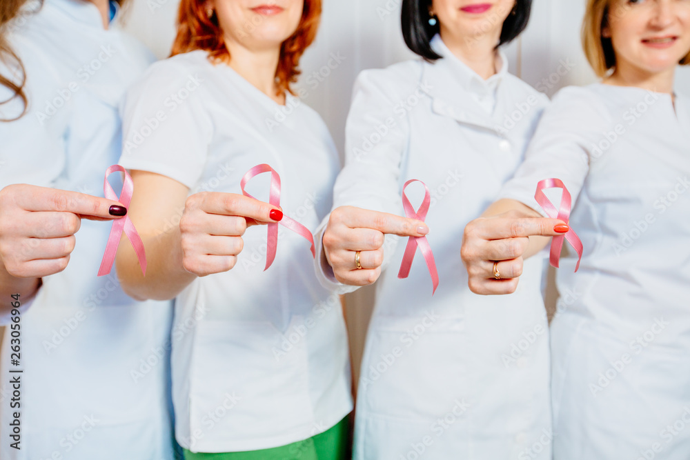 Close up of four hands unrecognizable female doctor in uniforms holding pink ribbons. Breast cancer awareness concept Close up of four hands unrecognizable female doctor in uniforms holding pink ribbons. Breast cancer awareness concept