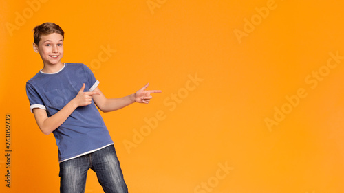 Cheerful teen boy pointing two fingers aside at free space