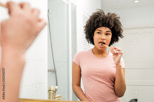 Woman brushing her teeth. Girl with bamboo brush in front of the mirror.