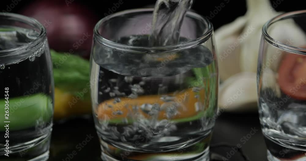 Pour alcohol vodka from a bottle in two shot glass. Background with vegetables Pour alcohol vodka from a bottle in two shot glass. Background with vegetables