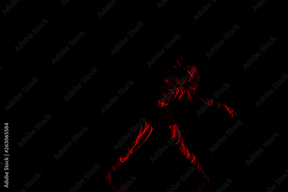 Ballet dancer dancing in front of and red light while expressing the hell with her magnificent dance moves. long exposure motion blur