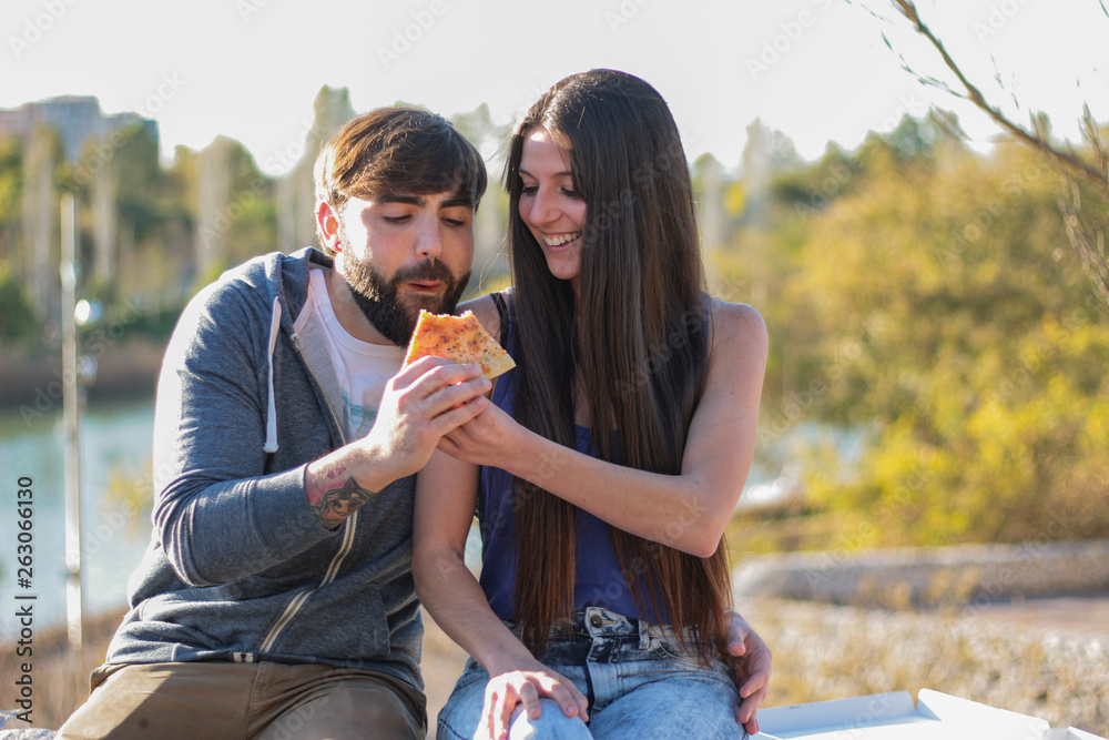 Fototapeta premium Couple eating pizza outdoors and smiling.They are sharing pizza