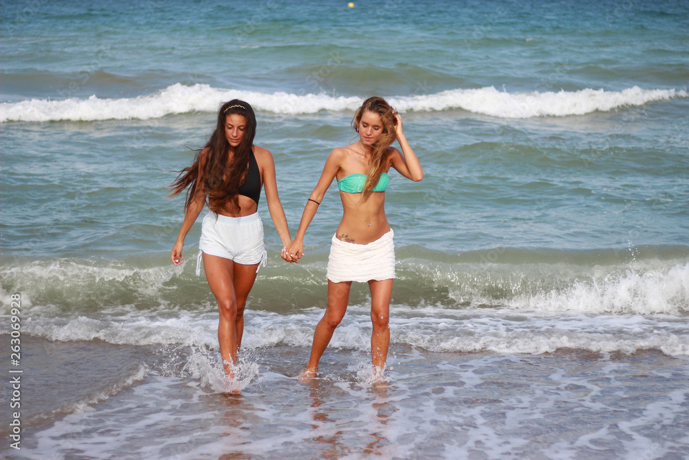 Two cute funny young girls are walking along the beach, laughing, having fun, crazy emotions, with bikini