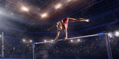 Female athlete doing a complicated exciting trick on horizontal gymnastics bars in a professional gym. Girl perform stunt in bright sports clothes
