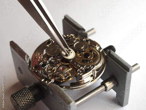 close up of watchmaker repairing old mechanical watch caliber taking small gear with tweezers photo