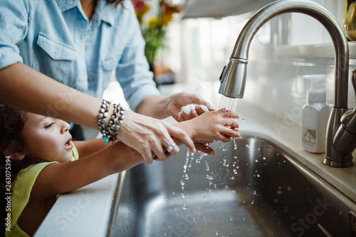 Mother and daughter washing hands in kitchen sink at home