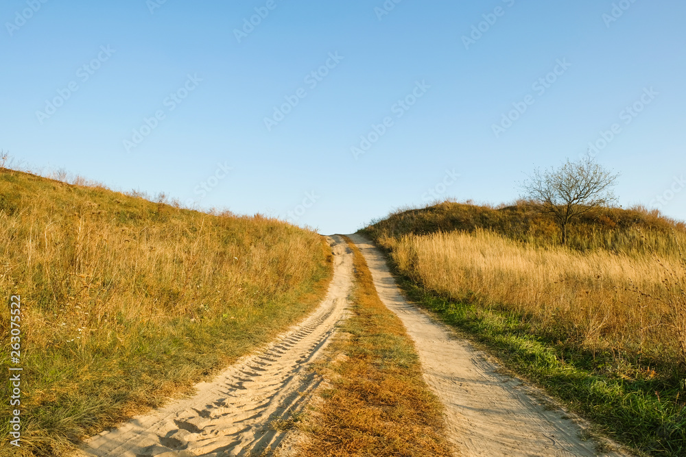 An imprint of tire trace on a sandy deserted  road up in the field of autumn evening in Ukraine. Copy space.         
