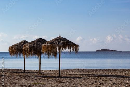 Beach umbrellas made of grass on sandy beach in Greece.