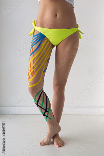 kinesiotaping the legs of the girl standing in front of a white wall in the Studio