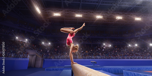 Female athlete doing a complicated exciting trick on gymnastics balance beam in a professional gym. Girl perform stunt in bright sports clothes photo