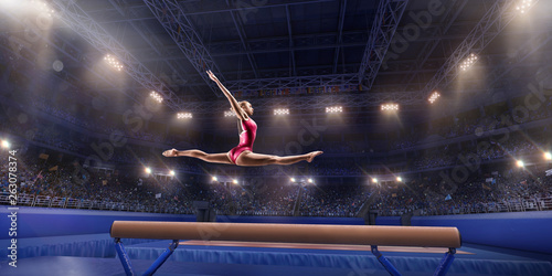 Female athlete doing a complicated exciting trick on gymnastics balance beam in a professional gym. Girl perform stunt in bright sports clothes photo