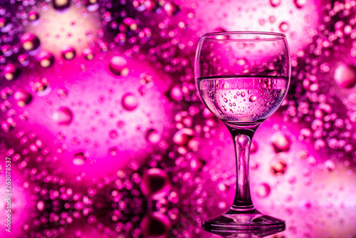 ransparent glasses with water and oily drops on colorful background 