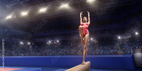 Female athlete doing a complicated exciting trick on gymnastics balance beam in a professional gym. Girl perform stunt in bright sports clothes © Alex